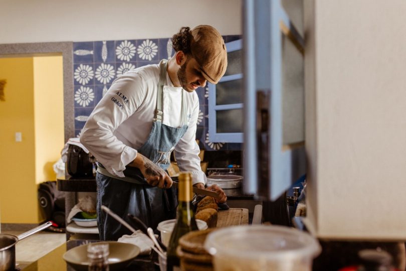 Técnico de controle de pragas inspecionando armário e rodapé de cozinha residencial